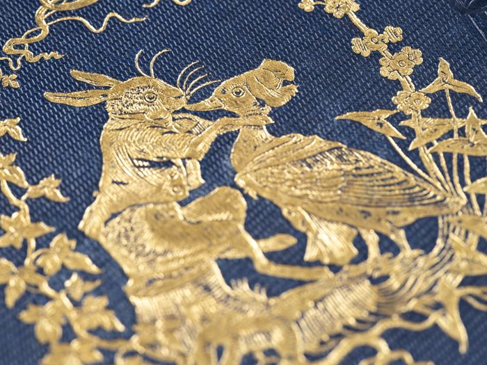 Broderie au fil d'or sur un tissu bleu représentant un lapin tenant un canard