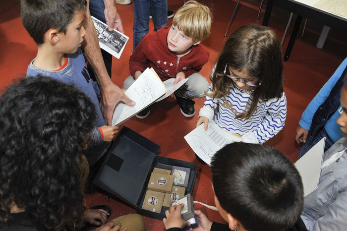 Au cours d’un périple au sein des Archives, les enfants s’amusent à plonger leurs mains de boîtes en boîtes et à découvrir les trésors des Archives du bout des doigts.